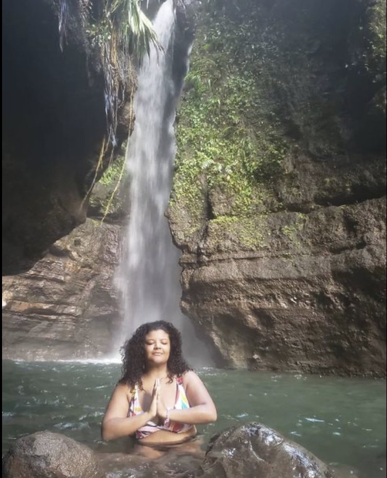 A person in a swimming pool with a natural waterfall in the background, practicing meditation with their hands in a prayer position.