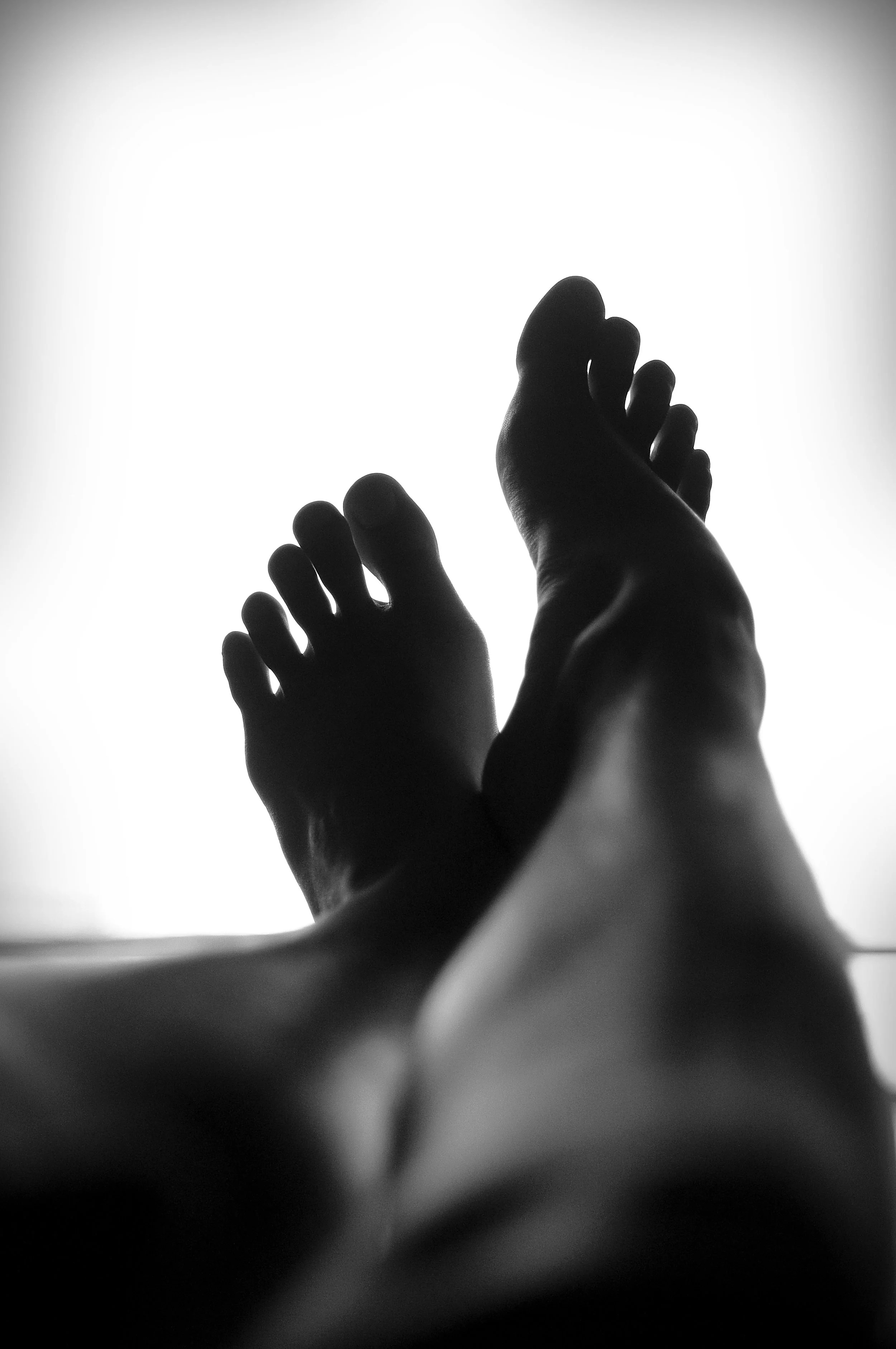 Close-up view of two feet positioned at an angle, with a bright light source in the background creating a silhouette effect.
