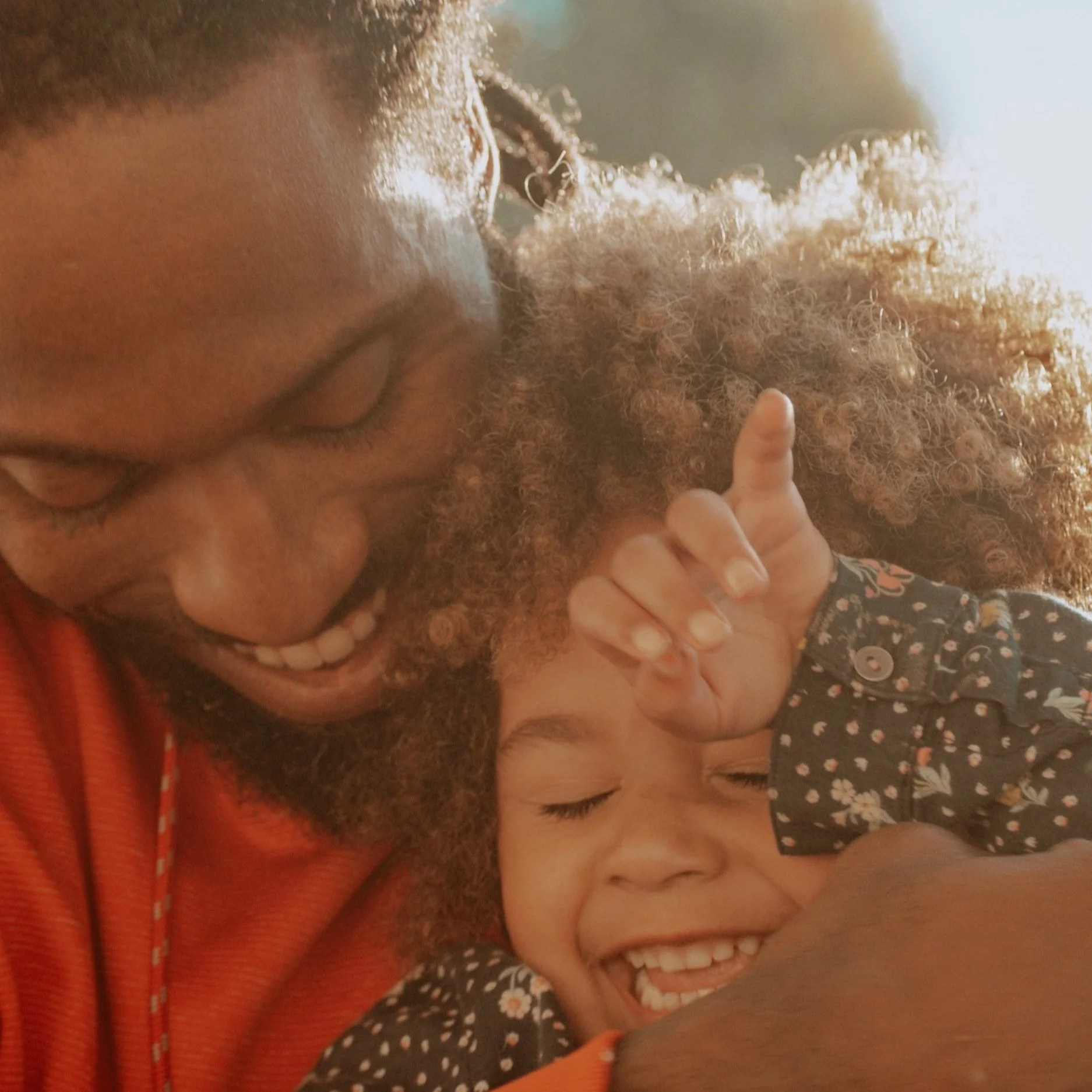 A joyful scene of a father embracing his smiling child, both showing happiness and affection in a sunlit outdoor setting.