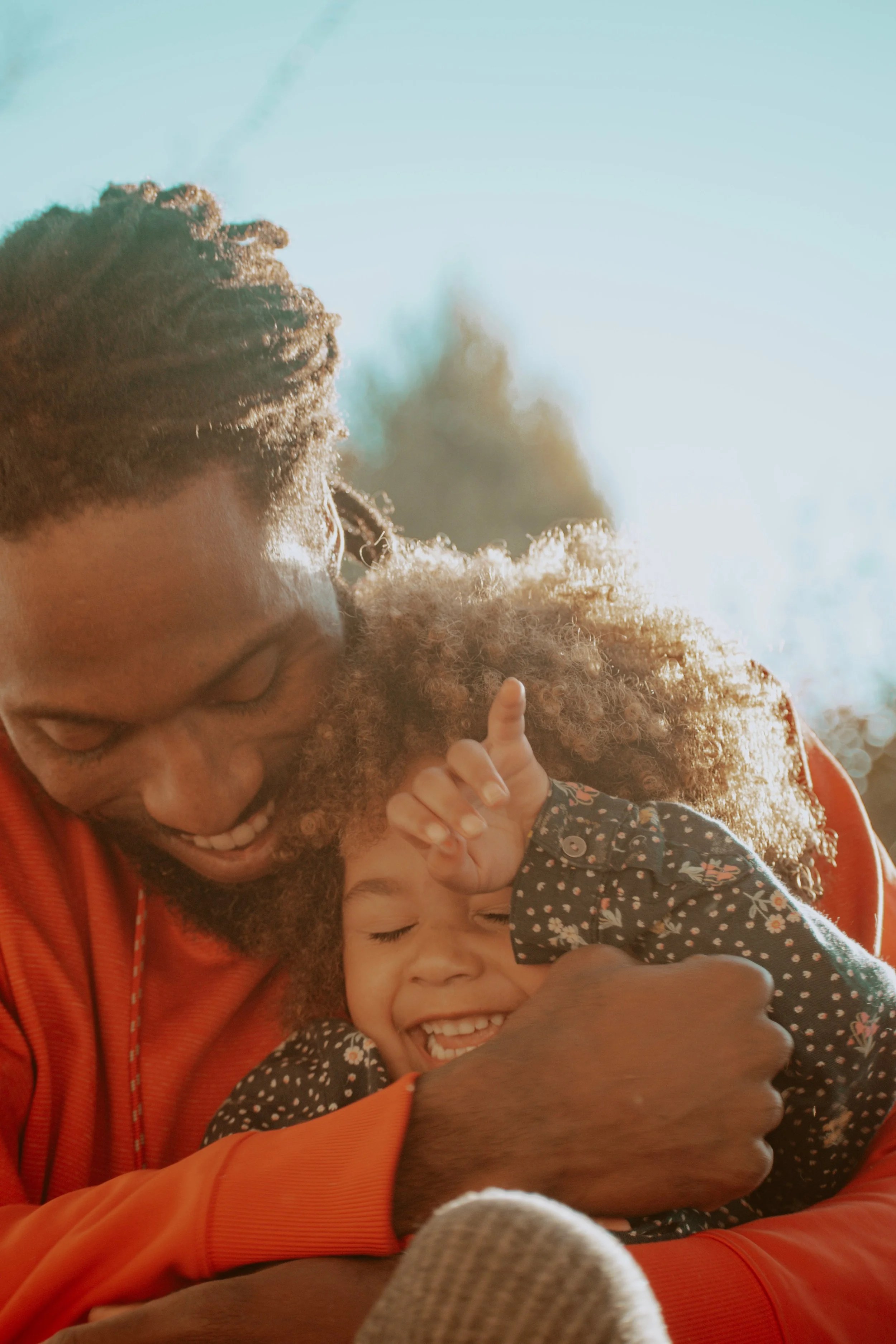 A joyful father gently embracing his smiling daughter outdoors, both sharing a moment of affection.