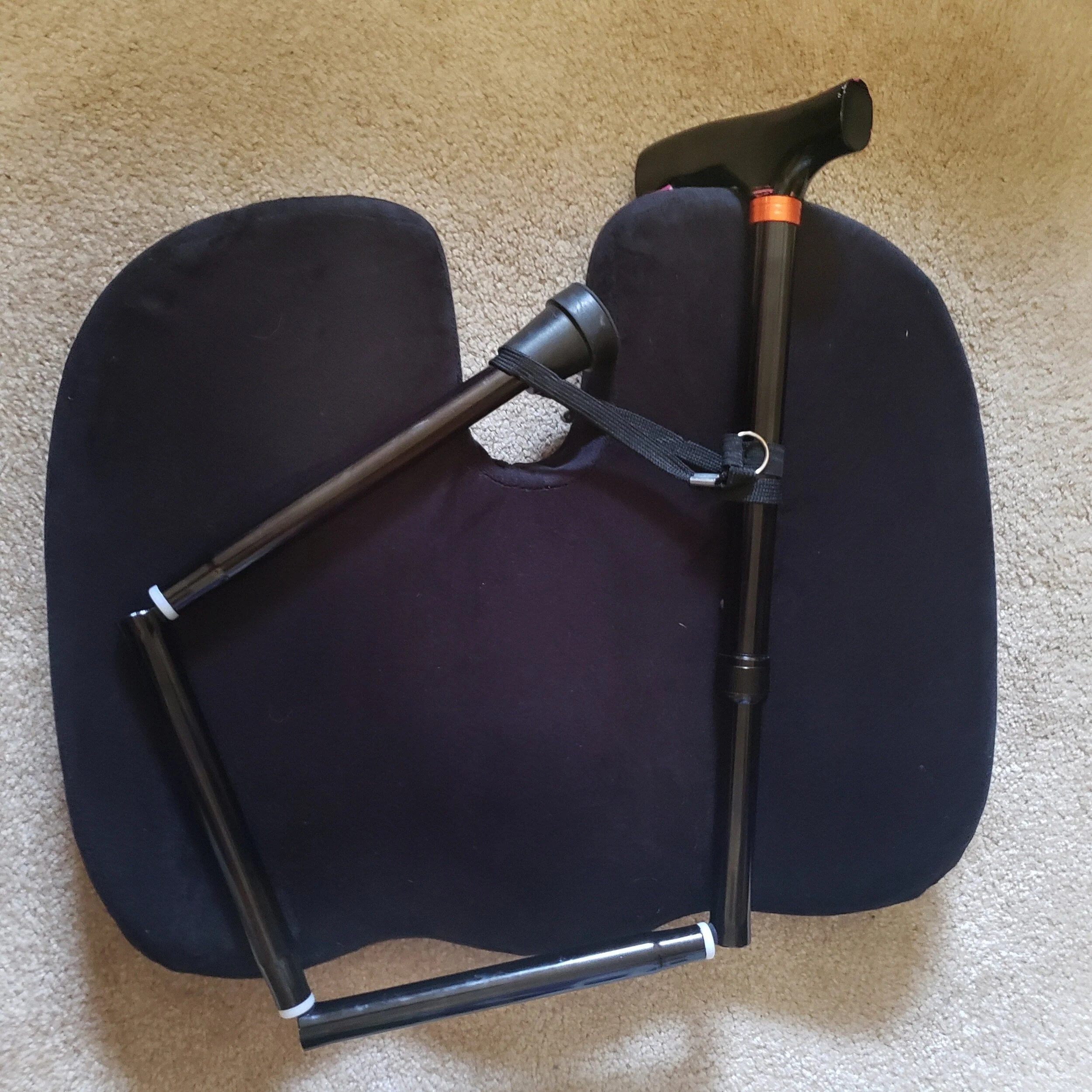 A folding cane resting on a black seat cushion, featuring a support strap.